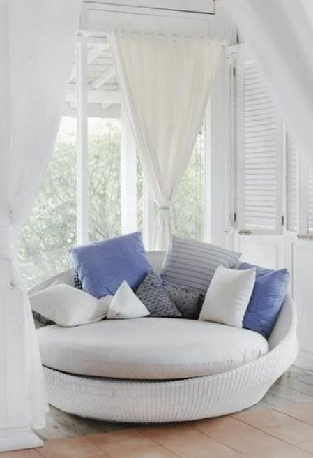 A white couch with blue pillows against the window with white curtains